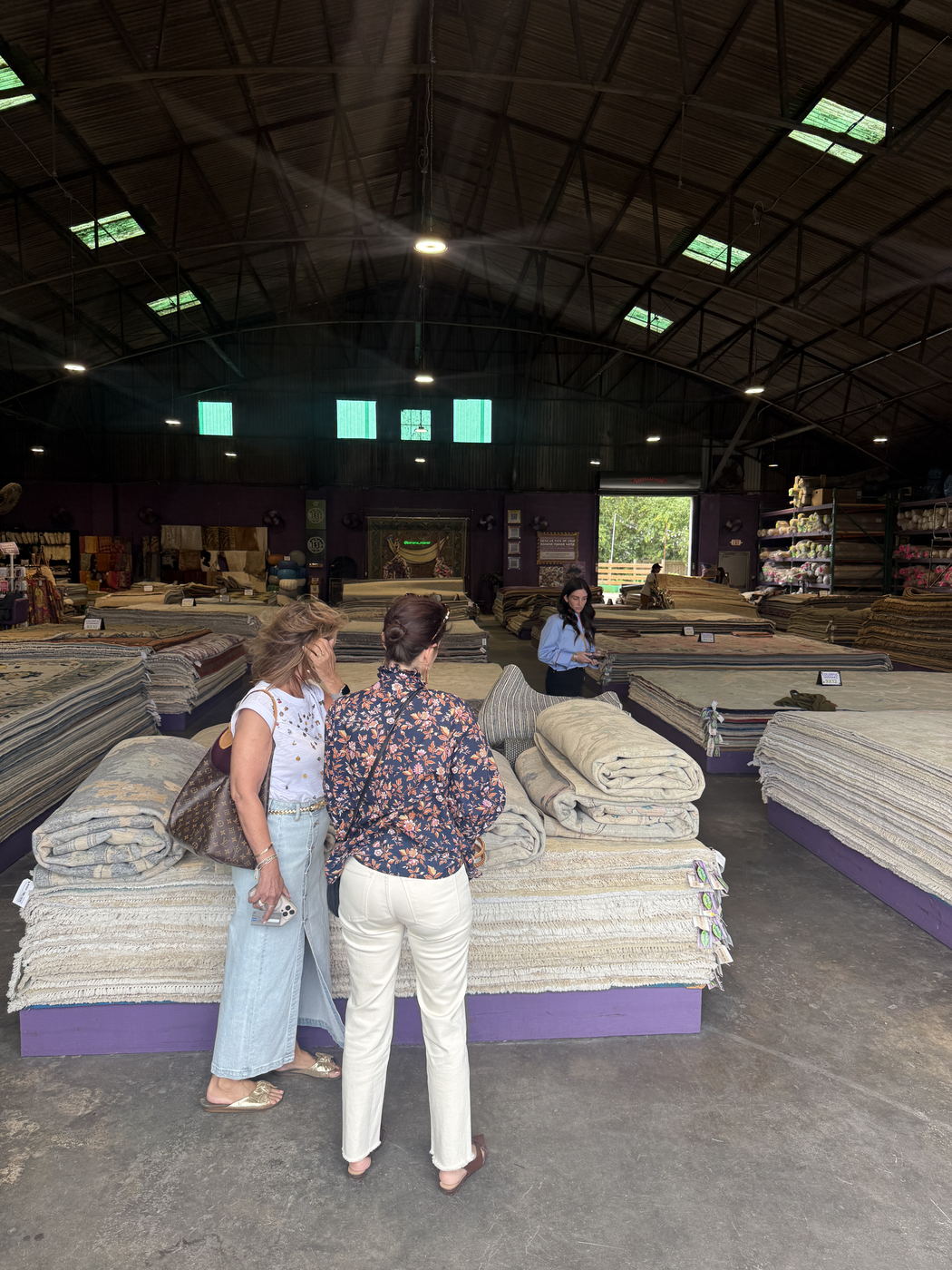 Two shoppers looking through stacks of hand-knotted rugs on the showroom floor